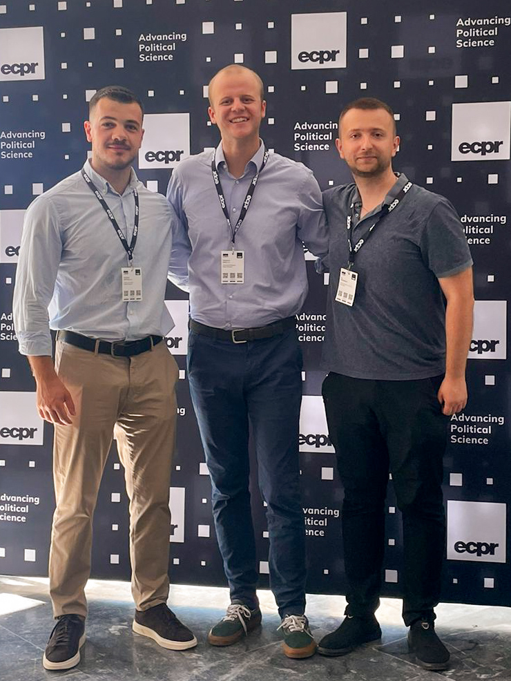 Scholars, Kledian Myftari, Ihor Moshenets (CEU) and Francesco Nasi (Bologna) standing in front of ECPR branded conference background