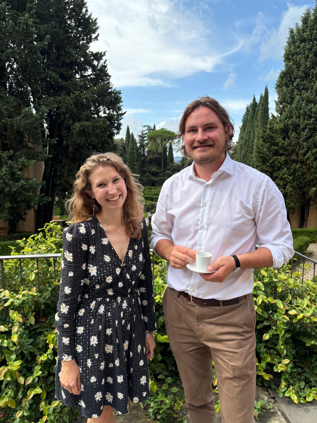 Scholars Florence and Topi standing in front of a green plants and trees