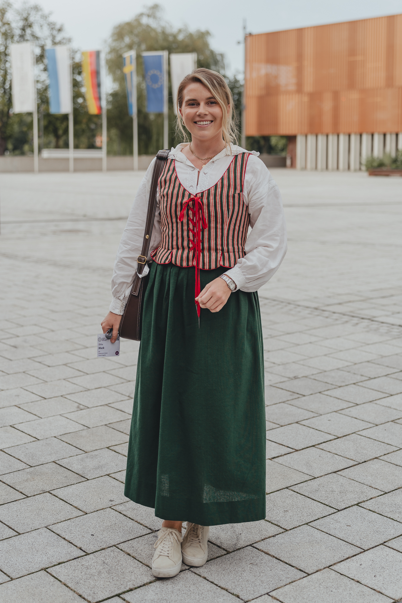 A young woman in traditional dress standing in front of a display of flags