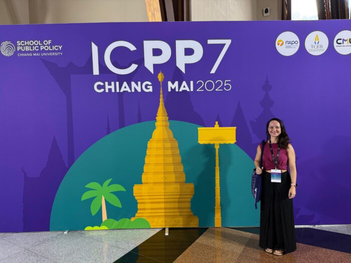 Scholar Julia Furtado (Luxembourg) standing in front of a purple conference branded background for the ICPP7 conference in Chiang Mai.